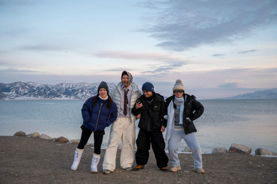 Four people stand on a rocky shore by a lake.
